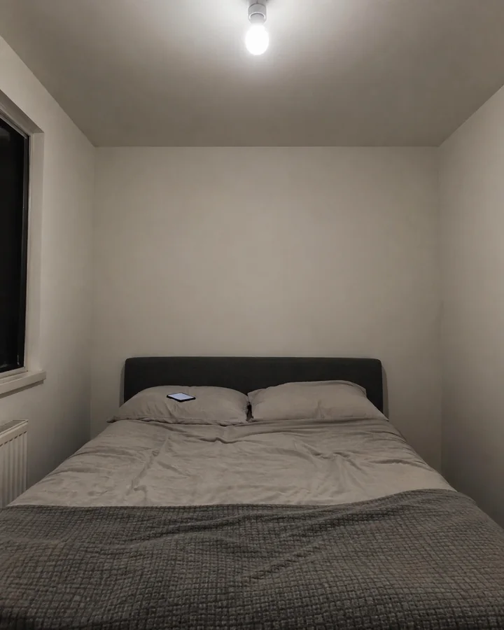 Quarto à noite iluminado só por uma lâmpada branca no teto, paredes vazias